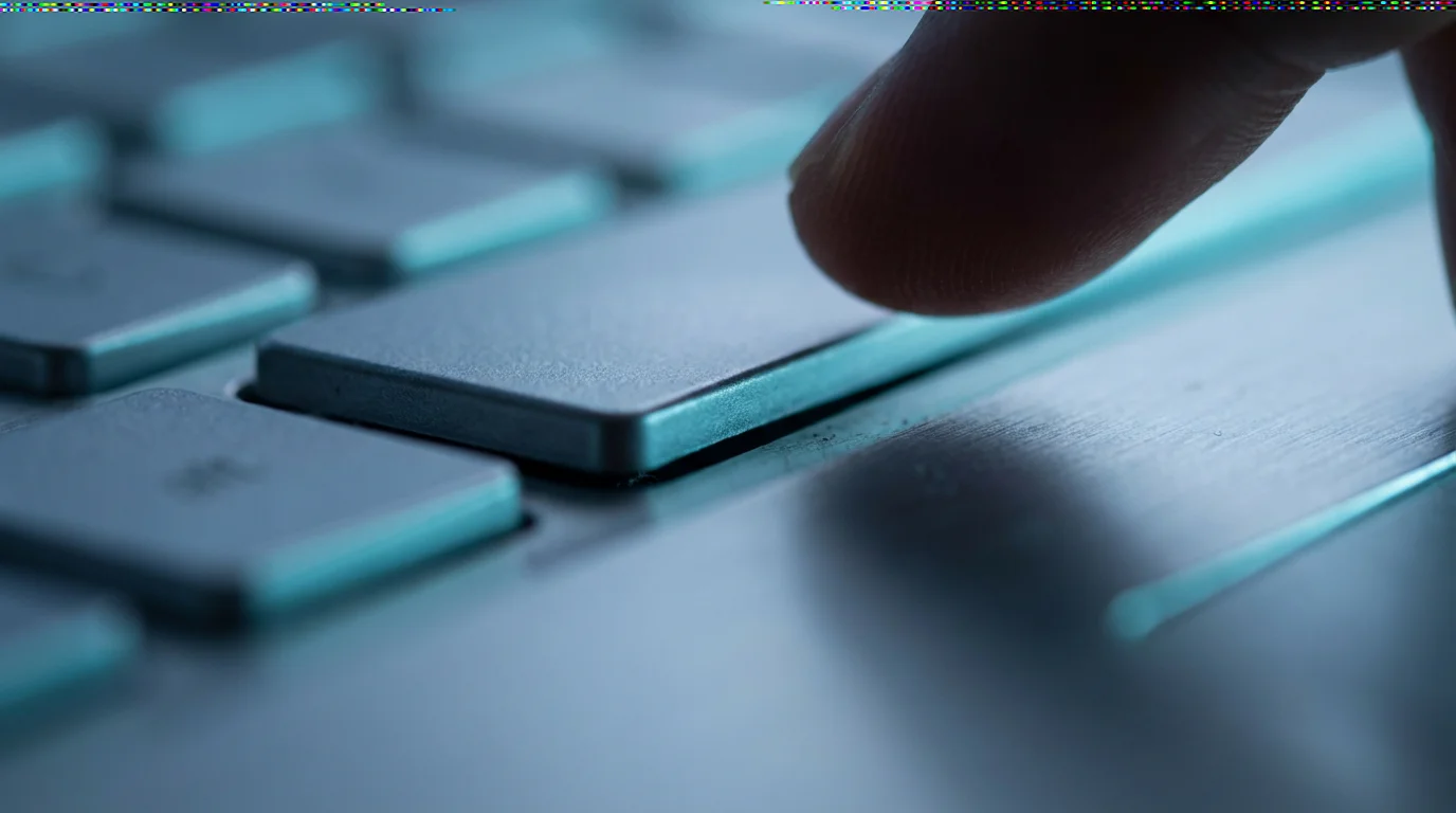 Macro photography of a finger pressing a silver laptop key in cool evening lighting.