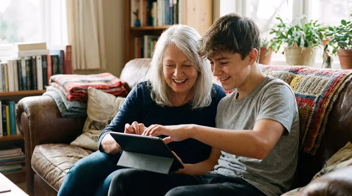 A teenager helping his grandmother set up her new tablet on a living room sofa.