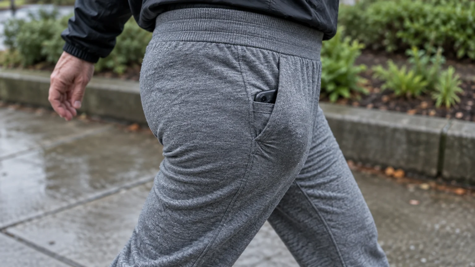 Side view of a person walking in gray sweatpants with a smartphone tucked into the front pocket.